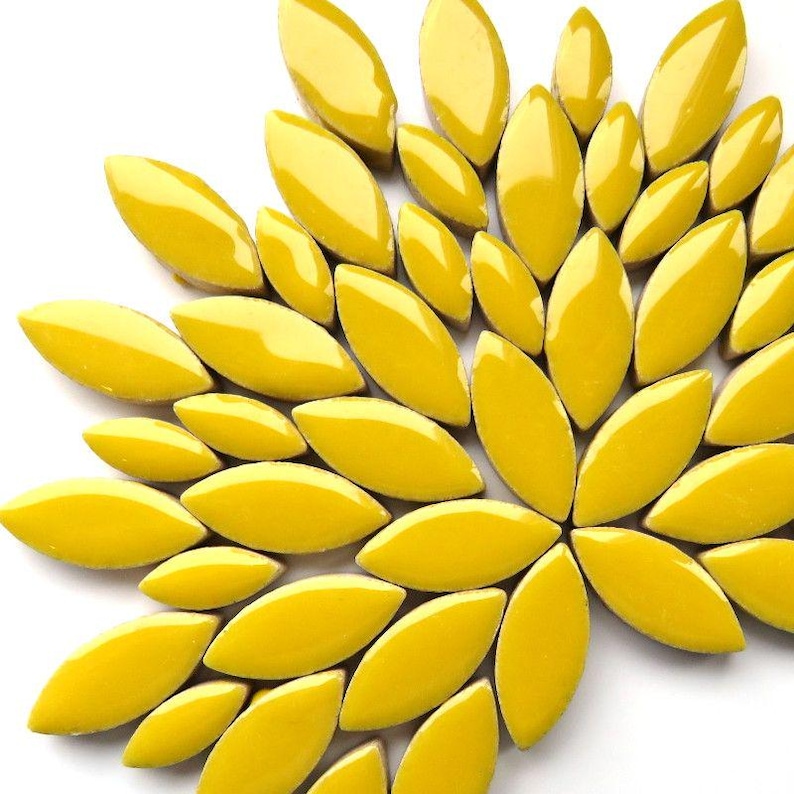 May include: A close-up of a decorative arrangement of glossy, yellow, leaf-shaped tiles. The tiles are arranged in a radial pattern, resembling a stylized flower or sunburst design. The bright yellow color and smooth texture create a visually appealing mosaic.