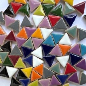 May include: A collection of colorful triangular tiles in various shades, including red, green, blue, yellow, and purple. Each tile is divided into two triangles of contrasting colors, creating a mosaic effect. The tiles are scattered on a white surface.