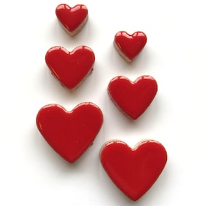 May include: Six glossy red heart-shaped objects of varying sizes are arranged on a white background. The hearts have a smooth, reflective surface and a light-colored edge. The arrangement suggests a theme of love or romance.