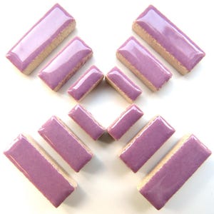 May include: A collection of rectangular ceramic tiles with a glossy lavender surface and a beige border. The tiles are arranged in a pattern, showcasing their shape and color. These tiles are suitable for various mosaic projects.