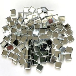 May include: A pile of small, square, mirrored glass tiles. The tiles are silver and reflect light, creating a shimmering effect. These mosaic tiles are ideal for craft projects and decorative applications.