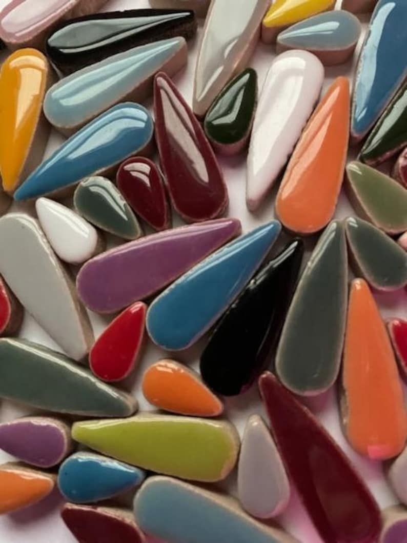 May include: A collection of colourful ceramic teardrop-shaped tiles in various shades of blue, green, red, orange, purple, and grey.