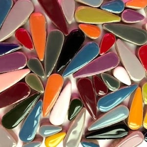 May include: A collection of colourful ceramic teardrop-shaped tiles in various shades of red, orange, yellow, green, blue, purple, brown, black, and white.