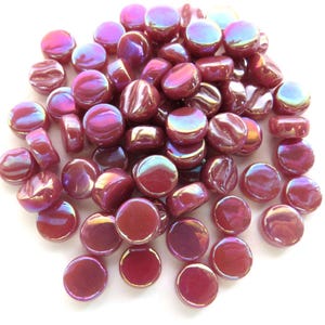 May include: A pile of iridescent, burgundy-colored glass mosaic tiles. The tiles are round and flat, with a glossy finish that reflects a rainbow of colors. These decorative tiles are ideal for craft projects.