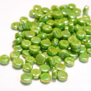 May include: A pile of small, round, iridescent green glass beads. The beads have a smooth, shiny finish and are perfect for crafting projects.