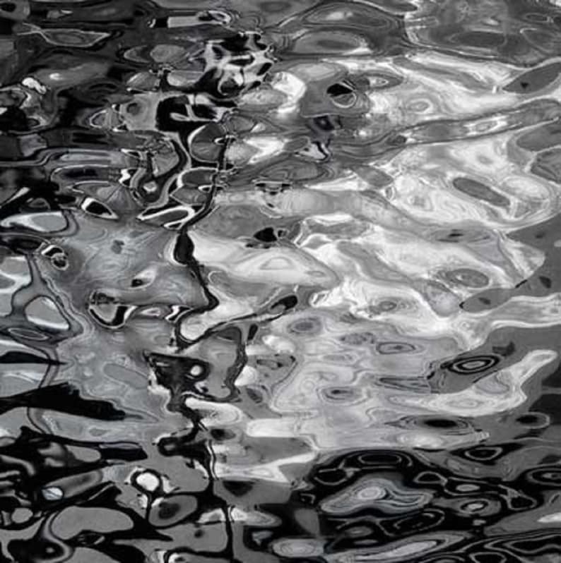 May include: Abstract black and white photograph of rippling water. The water is still and reflects the light, creating a pattern of swirls and circles.