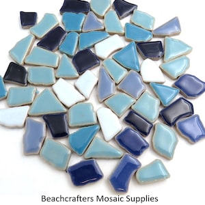 May include: A collection of irregularly shaped mosaic tiles in shades of blue, white, and navy. The tiles are glossy and appear to be ceramic. The text "Beachcrafters Mosaic Supplies" is at the bottom of the image.