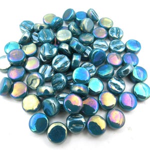May include: A collection of iridescent teal glass beads. The round beads have a flat, disc-like shape with a textured surface. The beads reflect a range of colors, including teal, blue, purple, and gold. These decorative beads are suitable for crafts and jewelry making.