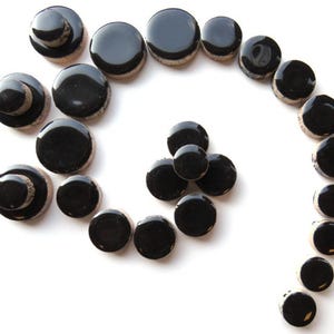May include: An assortment of black ceramic plugs and tunnels, arranged in a spiral pattern against a white background. The plugs vary in size and design, with some featuring a layered appearance.