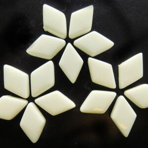 May include: Off-white diamond-shaped mosaic tiles arranged in three floral patterns against a black background. Each flower is composed of six tiles, creating a decorative design. The tiles have a glossy finish.