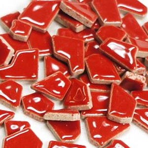 May include: A pile of irregularly shaped, glossy red ceramic tiles. The tiles have a bright red color with a white border and a rough, unglazed underside. The shapes vary, suggesting they are broken pieces.