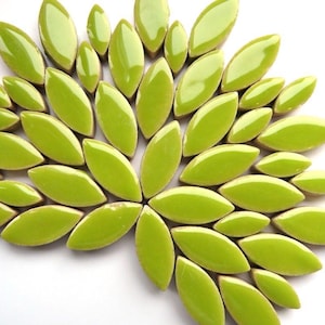 May include: A collection of glossy, lime green leaf-shaped tiles arranged in a radial pattern. The tiles have a smooth, reflective surface and are set against a white background. The design suggests a floral or botanical theme, suitable for decorative applications.