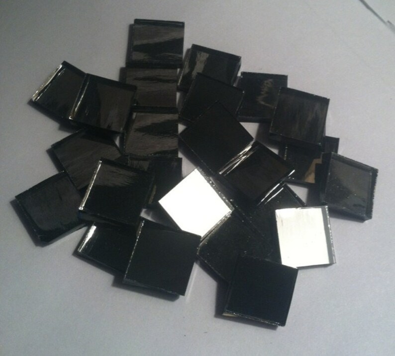 May include: A pile of black square mirror tiles. The tiles are arranged in a random pattern and some are slightly overlapping.