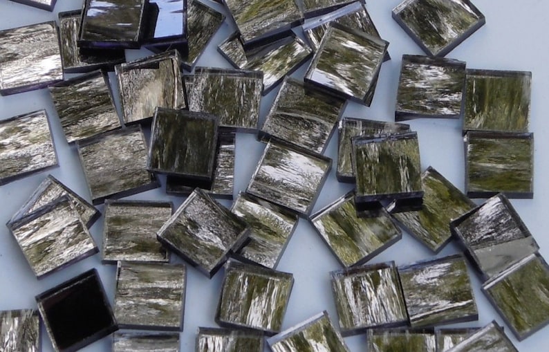 May include: A pile of small, square, green and silver mosaic tiles. The tiles have a metallic sheen and a textured surface.