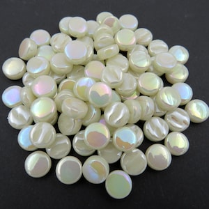 May include: A pile of iridescent white glass tiles. The tiles are round and have a smooth, glossy finish.
