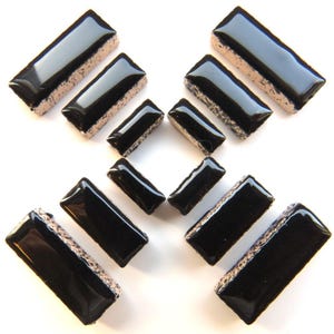 May include: Rectangular black glass tiles with a glossy finish and a textured, light-colored edge. The tiles are arranged in a scattered pattern, showcasing their shape and design. These tiles are suitable for various craft projects.
