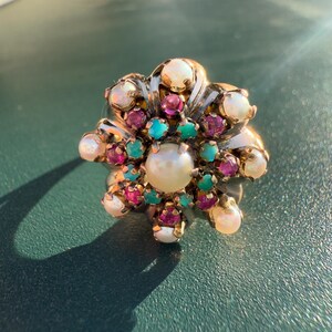 May include: A gold ring with a cluster of pearls, rubies, and turquoise gemstones. The ring has a floral design and is set in a gold band.