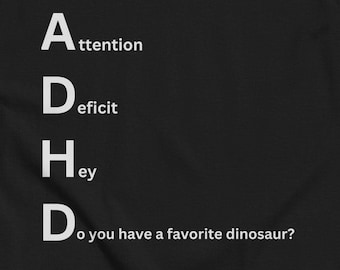 May include: Black t-shirt with white text that reads "ADHD: Attention Deficit Hey Do you have a favorite dinosaur?"