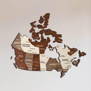 Könnte beinhalten: Eine mehrfarbige Holzwandkarte von Kanada mit beschrifteten Provinzen und Territorien. Die Karte verwendet verschiedene Braun- und Cremetöne des Holzes, um die geografischen Regionen über die gesamte Landmasse des Landes abzugrenzen.