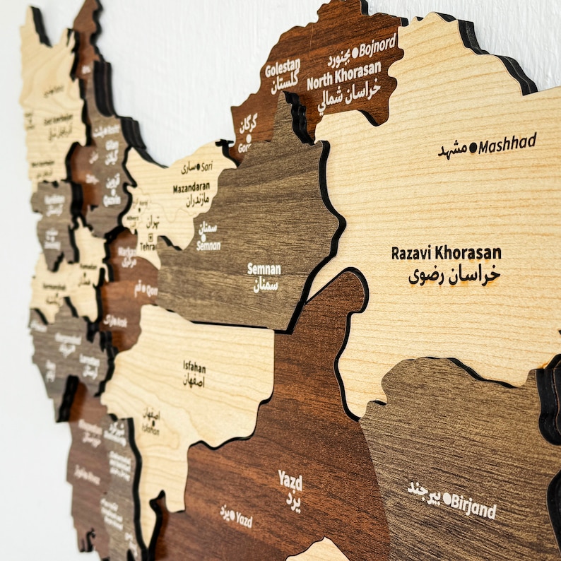 May include: A wooden map of Iran with the names of the provinces in both Farsi and English. The map is made of different shades of brown wood and has a black outline. The map is mounted on a white wall.