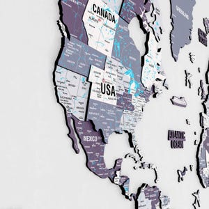 May include: A detailed, three-dimensional wall map of North America, including the USA, Canada, and Mexico. The map features individual state and province outlines in shades of gray and purple, with white text labels. The Atlantic Ocean is also labeled.