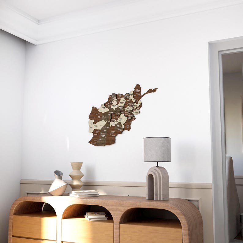 K&ouml;nnte beinhalten: Eine Holzkarte von Afghanistan mit den Namen der einzelnen Provinzen beschriftet. Die Karte ist an einer wei&szlig;en Wand &uuml;ber einem Holztisch mit einer Lampe und Dekorationsgegenst&auml;nden angebracht.