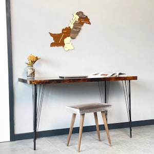 May include: A wooden desk with black hairpin legs and a matching stool. A wooden map of Pakistan hangs on the wall. A glass vase with flowers and a laptop are on the desk. An open book is also on the desk.