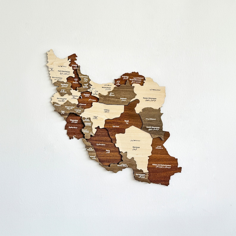 May include: A wooden map of Iran with each province outlined and labeled in both English and Farsi. The map is made of different shades of brown wood, giving it a rustic look.