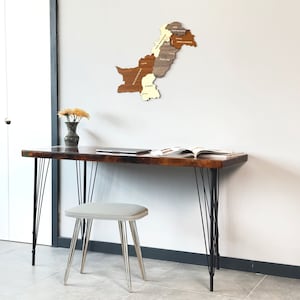 May include: A wooden desk with black hairpin legs and a matching stool. A wooden map of Pakistan hangs on the wall. A vase of yellow flowers and a laptop are on the desk. An open book is also on the desk.