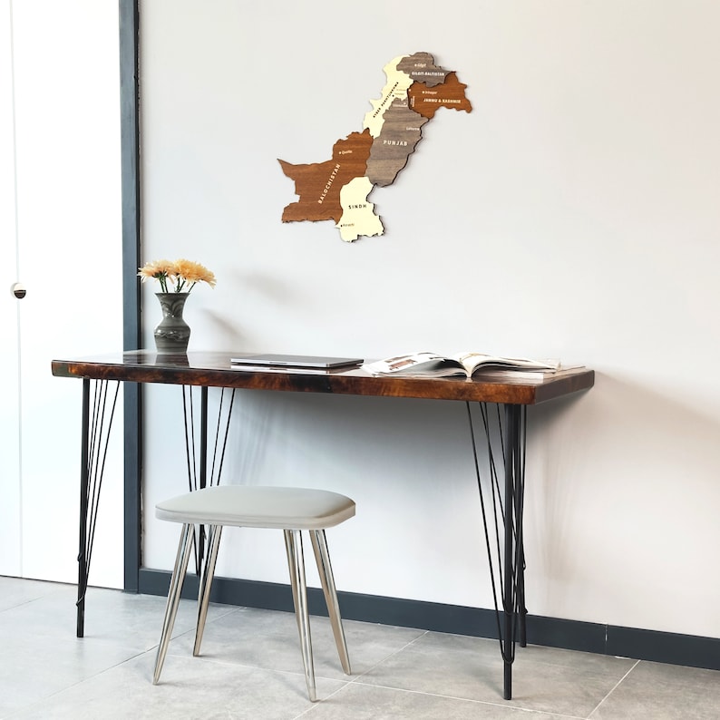 May include: A wooden desk with black hairpin legs and a matching stool. A wooden map of Pakistan hangs on the wall. A vase of yellow flowers and a laptop are on the desk. An open book is also on the desk.