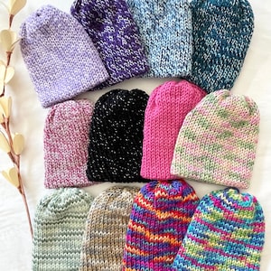 May include: A collection of 12 knitted hats in various colors and patterns, including black, pink, green, blue, purple, and brown.