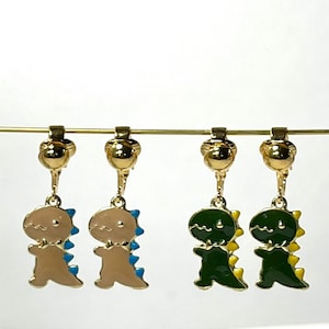 May include: Four gold clip-on earrings with dinosaur charms. Two earrings feature a brown dinosaur with blue and yellow accents. The other two earrings feature a green dinosaur with yellow accents.