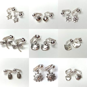 May include: Assortment of silver clip-on earrings with various charms, including stars, hearts, butterflies, Hello Kitty characters, birds, suns, and ladybugs.