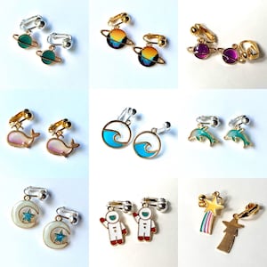 May include: A set of 10 pairs of clip-on earrings featuring various designs, including planets, whales, waves, dolphins, stars, and astronauts. The earrings are made of metal and have a gold or silver finish.