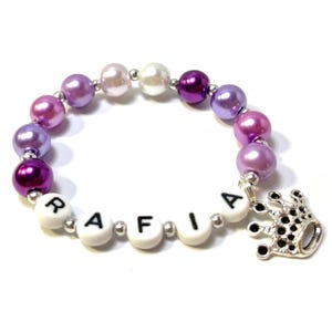 May include: A purple, pink, and white beaded bracelet with a silver crown charm and the name "RAFIA" spelled out in black letters on white beads.