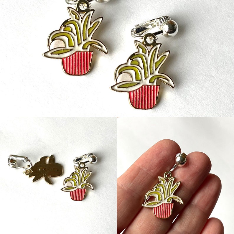 May include: A pair of gold-tone clip-on earrings featuring a green plant in a red pot. The earrings are made of metal and have a shiny finish.