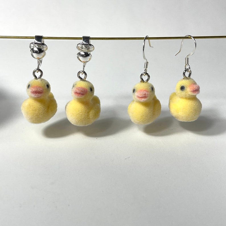 May include: Four yellow duck earrings with silver hooks and clasps. Two of the earrings are clip-on style.