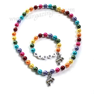 May include: Rainbow beaded necklace and bracelet set with a unicorn charm. The bracelet has the name "MADDY" spelled out in white letters.