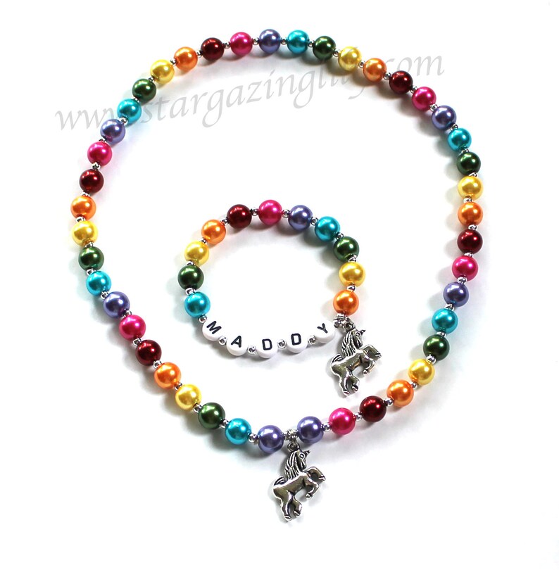 May include: Rainbow beaded necklace and bracelet set with a unicorn charm. The bracelet has the name "MADDY" spelled out in white letters.