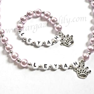 May include: A pink and silver beaded necklace and bracelet with the name "LEYAH" spelled out in white letters and a silver crown charm.