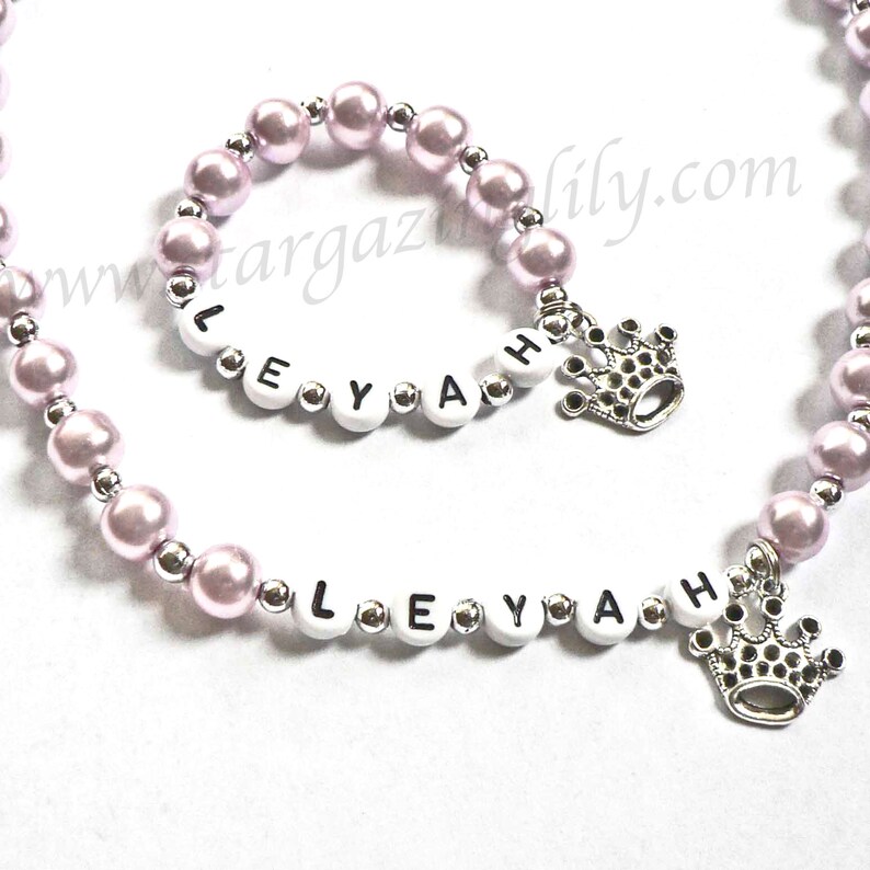 May include: A pink and silver beaded necklace and bracelet with the name "LEYAH" spelled out in white letters and a silver crown charm.