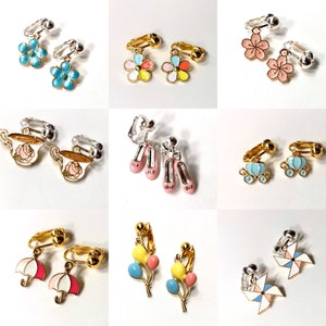 May include: Assortment of colorful clip-on earrings featuring various designs, including flowers, teacups, ballet shoes, balloons, and windmills.