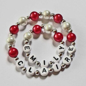 May include: Two bracelets with alternating red and white beads, spelling out the names "Claire" and "Emily" in black letters.