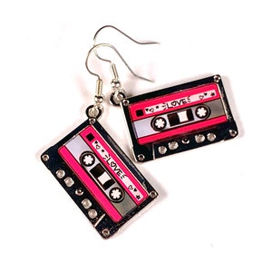May include: A pair of silver cassette tape earrings with pink and white details. The cassette tapes have the text "<3 LOVE" on them.