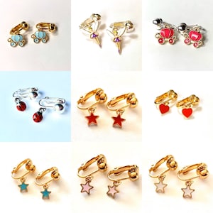 May include: Assortment of clip-on earrings with various charms, including stars, hearts, ladybugs, fairies, and carriages. The earrings are gold-toned with colorful enamel accents.