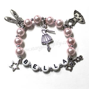 May include: A pink beaded bracelet with silver charms, including a ballerina, a star, a shoe, a dress, and the word "Dance". The bracelet also has white beads with the letters "BELLA" on them.