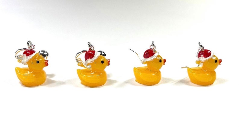 May include: Four pairs of yellow rubber ducky earrings with red and white Santa hats. The earrings are silver and have a hook closure.