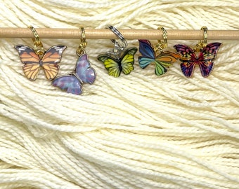 May include: Five colorful butterfly stitch markers on a wooden knitting needle. The butterflies are purple, yellow, green, red, and orange.