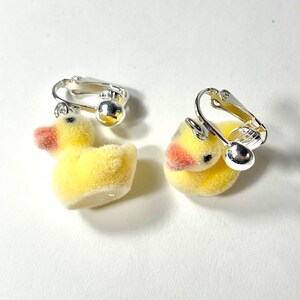 May include: A pair of yellow rubber ducky clip-on earrings. The ducks are made of soft, fuzzy material and have a silver clip-on backing.