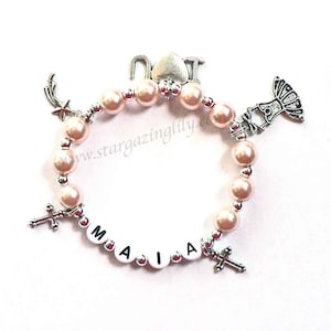 May include: A pink beaded bracelet with silver charms, including a cross, a star, a ballerina, and the letters "NOT" and "MAIA".